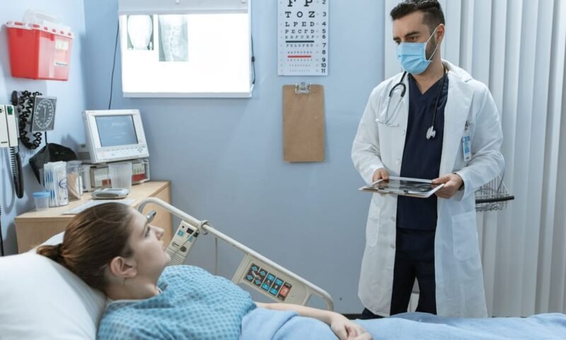 Doctor wearing face mask consulting with a patient in a hospital room, highlighting healthcare safety.