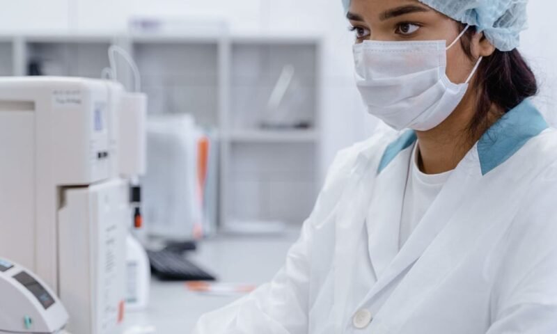 A female scientist wearing PPE works focused in a modern laboratory setting.